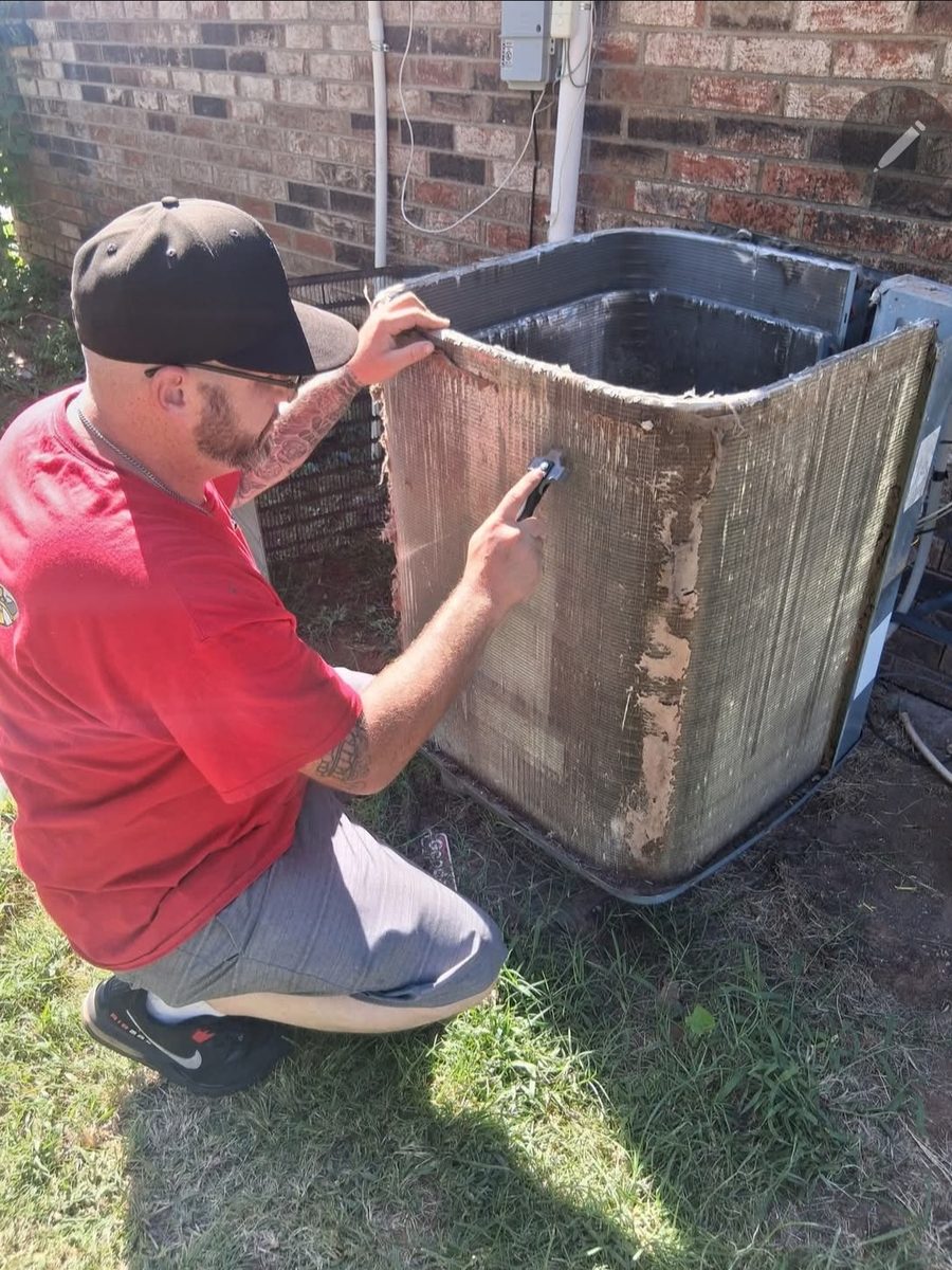 HVAC technician cleaning and straightening condenser coil fins during maintenance
