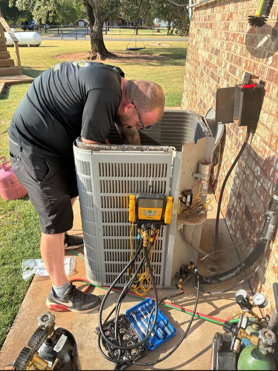 HVAC technician servicing an outdoor AC condenser with digital manifold gauges