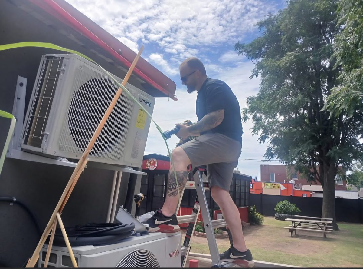 HVAC technician installing an outdoor mini-split condenser unit on a building exterior