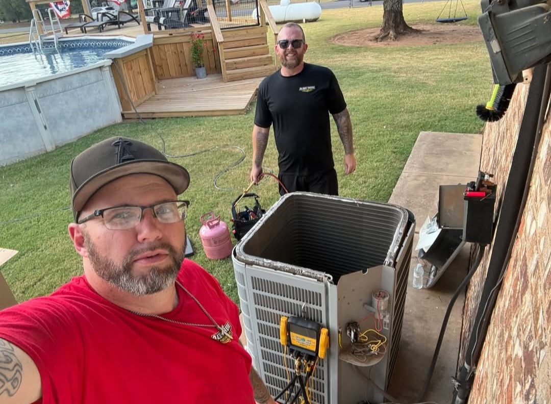 Two HVAC technicians servicing an outdoor condenser unit with refrigerant gauges